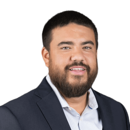 A man with a beard wearing a suit and striped shirt poses against a plain background.